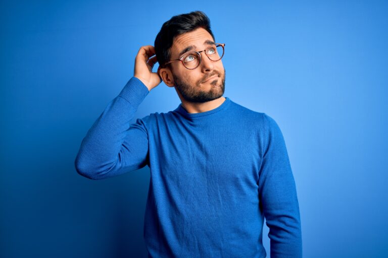 Young handsome man with beard wearing casual sweater and glasses over blue background confuse and wondering about question. Uncertain with doubt, thinking with hand on head. Pensive concept